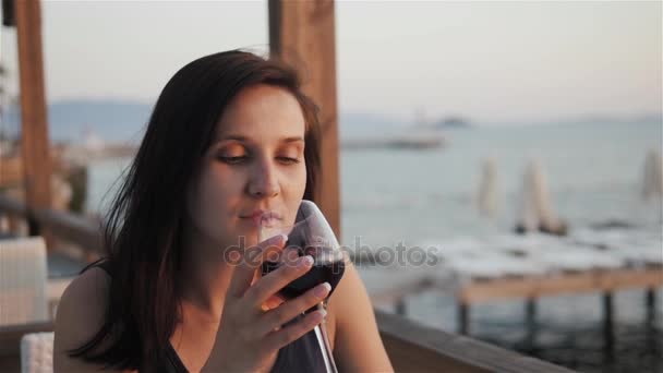 Jeune femme buvant du vin rouge sur une terrasse extérieure regardant un beau coucher de soleil sur la mer — Video