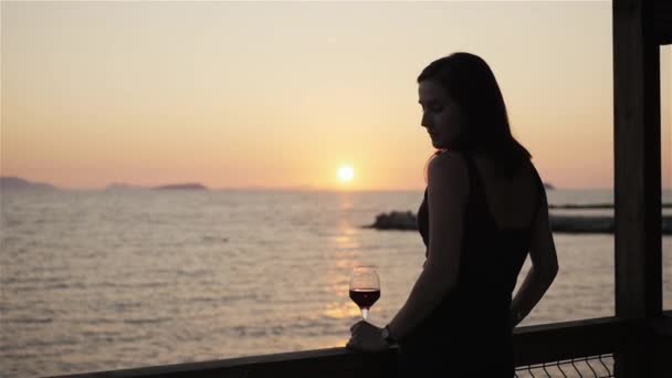 Silhouet van jonge vrouw drinken van rode wijn op buiten terras mooie zonsondergang uitzicht op de zee kijken — Stockvideo