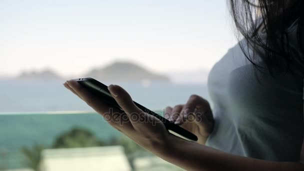Νεαρή γυναίκα που χρησιμοποιούν Tablet Pc να στέκεται δίπλα στο παράθυρο με θέα βουνών και θάλασσας — Αρχείο Βίντεο