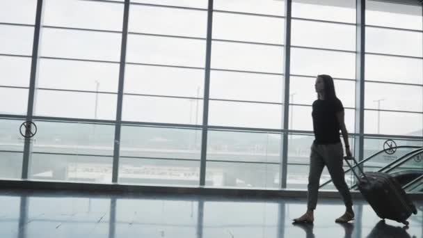 年轻漂亮的商业妇女的剪影在机场走她的行李, 而等待她的排队登记, 旅游概念 — 图库视频影像