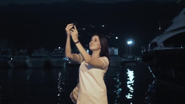 Yong Woman Tirando fotos por Smartphone. Mulher viajante elegante do verão com telefone ao ar livre na cidade europeia, baía da noite com iates no fundo — Vídeo de Stock