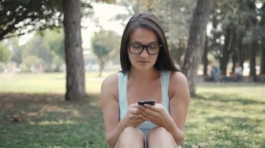 Telefonu kullanarak, On-line alışveriş kavramı Park'ın bahçesinde oturan genç güzel kız portresi kapatın