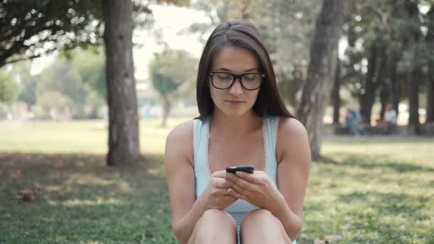 Portré, fiatal, gyönyörű lány ül a gyep a Park segítségével telefonon, On-line vásárlás koncepció közelről — Stock videók