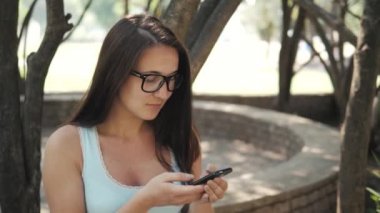 Güneşli bir günde bir parkta bir bankta oturmuş, On-line alışveriş kavramı bir akıllı telefon ile güzel neşeli kız