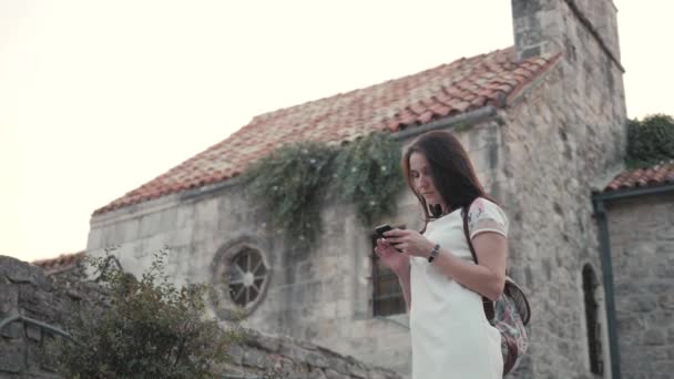 Портрет молодой женщины с использованием смартфона, путешествия с рюкзаком, стильный повседневный наряд, вечерний закат — стоковое видео