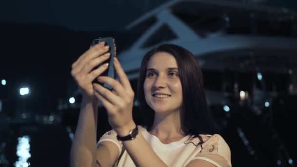 Yong Frau fotografiert mit dem Smartphone. stilvolle Sommerreisende Frau mit Telefon im Freien in der europäischen Stadt, Nachtbucht mit Yachten im Hintergrund — Stockvideo