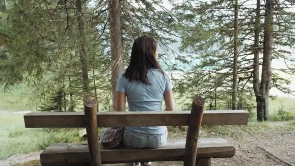 Menina descansando em um banco junto ao lago com vista para as montanhas e a floresta. Menina admira o lago e montanhas — Vídeo de Stock