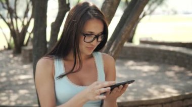 Güneşli bir günde bir parkta bir bankta oturmuş, On-line alışveriş kavramı bir Tablet Pc ile güzel neşeli kız