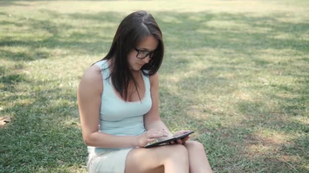 Menina bonita nova sentada no gramado no parque usando Tablet PC, conceito de compras on-line — Vídeo de Stock