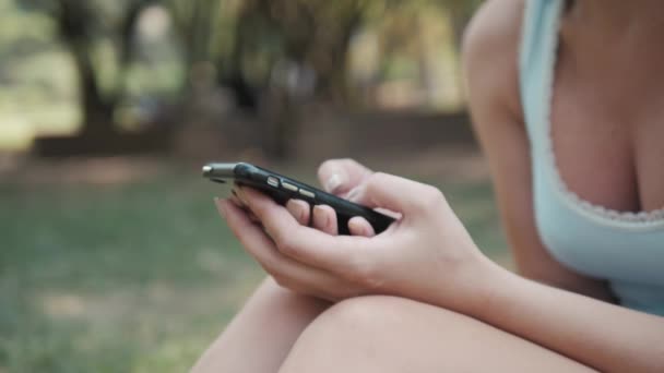 Крупный план молодой красивой девушки, сидящей на лужайке в парке с помощью телефона, он-лайн концепции покупок — стоковое видео