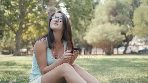 Молодая красивая девушка сидит на лужайке в парке с помощью телефона, он-лайн концепция покупок — стоковое видео