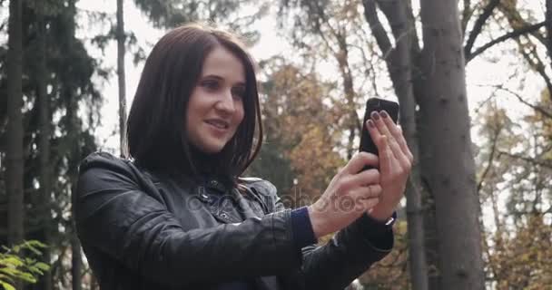 Krásná mladá brunetka žena užívat Selfie pomocí Smartphone. Zblízka šťastná dívka pomocí Smartphone venku podzim — Stock video