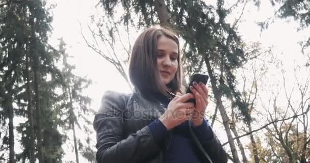 美しい若いブルネット女性のスマート フォンを使用して Selfie を撮影します。秋に屋外でスマート フォンを使用して幸せな女の子のクローズ アップ — ストック動画