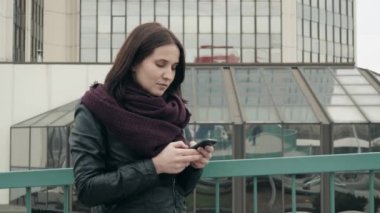 Çekici turist kasabasında, hippi kız cep telefonu aracılığıyla da kentsel ayarı promosyon arka plan manifatura iletilerde ayakta gezinmek için Smartphone uygulama kullanarak rahat kıyafet giymiş