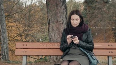 Parkta bankta oturmuş smartphone kullanan genç gülümseyen kadın. Güzel Avrupa kız manifatura telefon