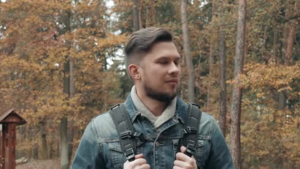 Retrato do jovem barbudo na floresta de outono com uma mochila turística, estilo de outono, estilo de vida itinerante — Vídeo de Stock