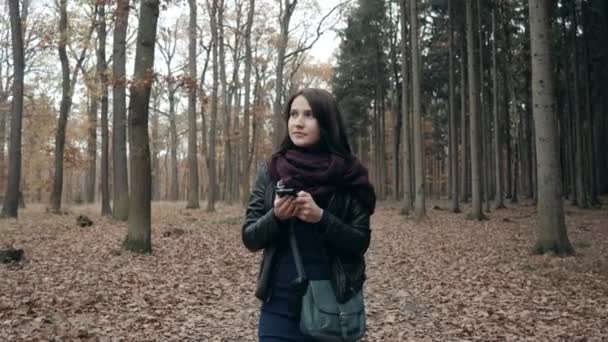 Hermosa joven morena mujer usando Smartphone en otoño Park. Chica caminando en el bosque en otoño, concepto de estilo de vida — Vídeo de stock