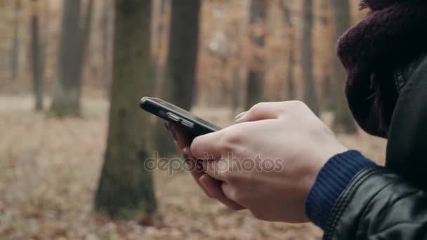 在秋季公园用智能手机关闭女人的手。秋天的女孩在森林漫步, 生活方式概念 — 图库视频影像