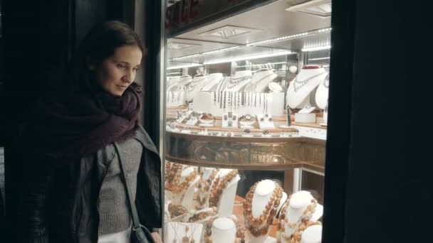 Mujer joven en paños de otoño mira en el escaparate con joyas en la calle de la noche — Vídeo de stock