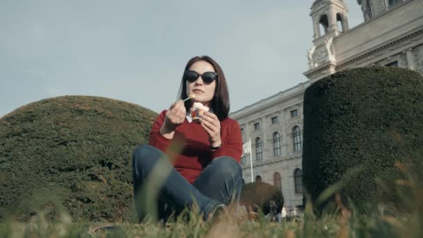 Счастливая молодая женщина наслаждается мороженым, сидя на траве в парке в солнечный день — стоковое видео