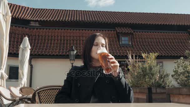 Genç kadın bir sokak restoranda bardak bira içme. Kız bir Cafe sokakta bira güneşli bir günde hoşlanır. — Stok video