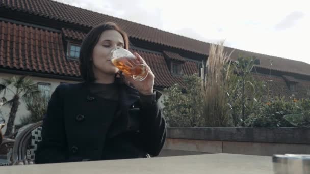 Wanita muda meminum gelas bir di restoran pinggir jalan. Girl Enjoys Beer In a Cafe On The Street On a Sunny Day — Stok Video