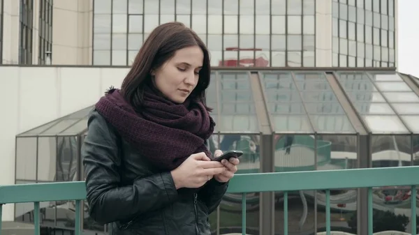 Atrakcyjnej, ubrany w odzież codzienna, przy użyciu aplikacji na smartfona do nawigowania w miasto, Hipster dziewczynę stojącą na miejskich ustawienie tła promocyjne SMS wiadomości za pomocą telefonu komórkowego Obrazy Stockowe bez tantiem