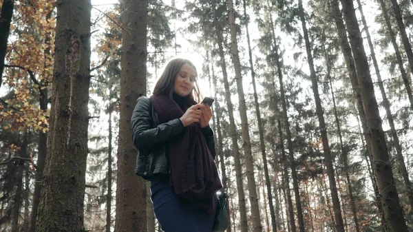 Bella Giovane Bruna Donna Utilizzando Smartphone In Autunno Parco. Ragazza che cammina nella foresta in autunno, concetto di stile di vita Foto Stock