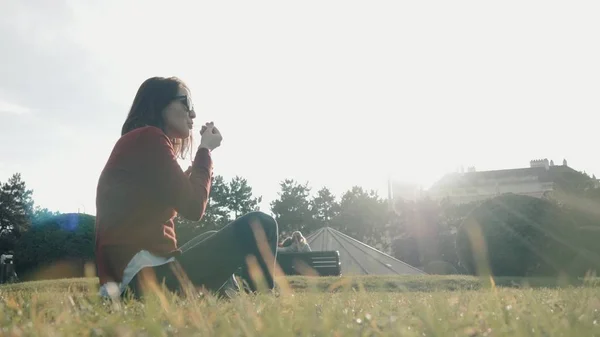 Felice giovane donna godendo di un gelato seduto sull'erba al parco in un giorno soleggiato Immagine Stock
