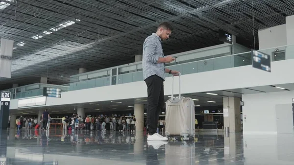 Bello giovane che usa lo smartphone e lavora in aeroporto in attesa della sua coda per la registrazione, il concetto di viaggio, la tecnologia Immagine Stock