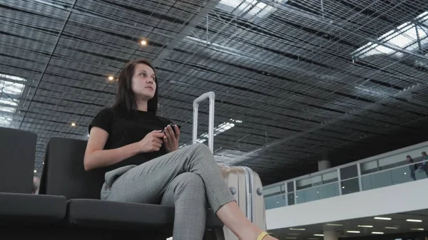 Молода красива бізнес-леді, використовуючи смартфон в аеропорту, чекаючи її черги для реєстрації, концепція подорожі Ліцензійні Стокові Зображення
