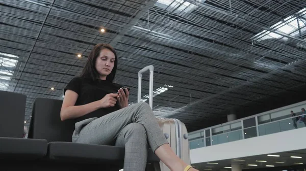 Giovane bella donna d'affari utilizzando uno smartphone in aeroporto in attesa della sua coda per la registrazione, Viaggiare concetto Foto Stock