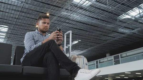 Красива молода людина використовує смартфон і працює в аеропорту, чекаючи його черги для реєстрації, концепції подорожей, технології Ліцензійні Стокові Зображення