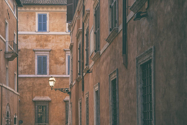 Street lamp on the wall of an old house against the backdrop of facades with windows in the city of Rome