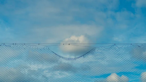 Wolken am blauen Himmel in der Nähe der Gitterbarriere — Stockfoto