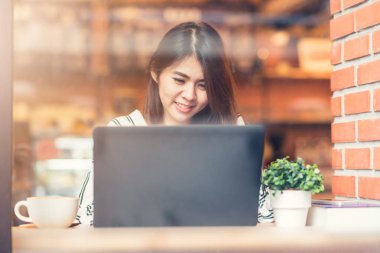 Asyalı kadın gülümseme kafede dizüstü bilgisayar ile çalışırken
