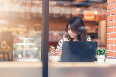 Asyalı kadın gülümseme kafede dizüstü bilgisayar ile akıllı telefon telefon kullanırken