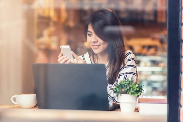 Asiatisk kvinna leende medan du använder smart telefon mobil med laptop på café — Stockfoto
