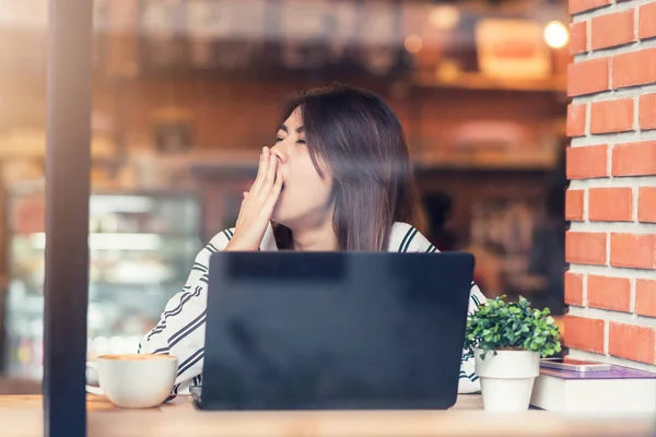 Sömnig ung asiatisk kvinna gäspar medan du använder laptop på café — Stockfoto