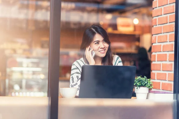 Asiatisk kvinna leende medan du använder smart telefon mobil med laptop på café — Stockfoto