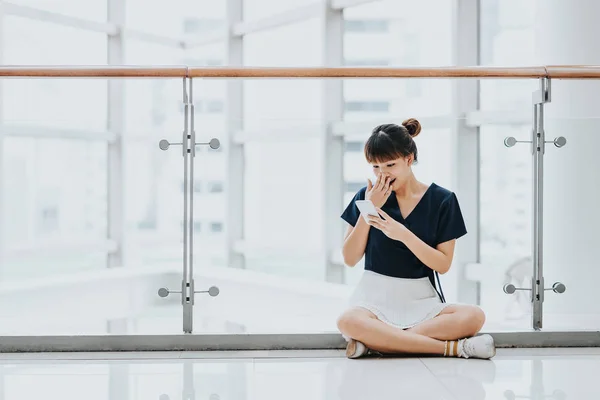 Menina asiática jovem surpreso enquanto sentado e usando telefone inteligente — Fotografia de Stock