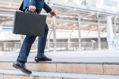 Deri evrak çantası yukarı merdiven üzerinde yürürken tutan işadamı 
