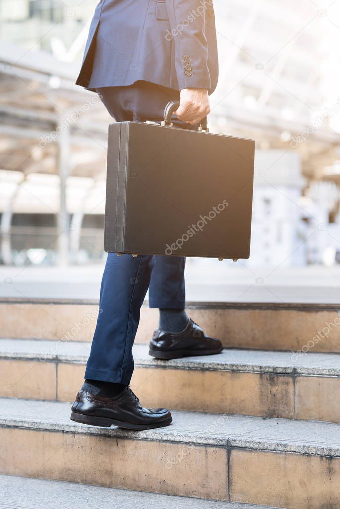 businessman holding leather briefcase while walking upward on the stair 
