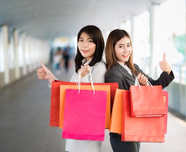 Asyalı kadın ortaya başparmak alışveriş çantası tutarken