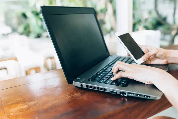 Hand med hjälp av bärbar dator och smartphone — Stockfoto