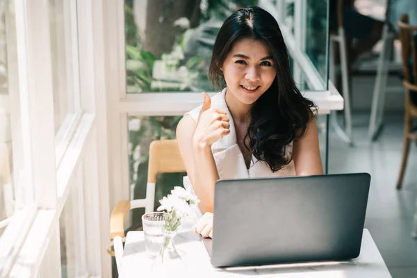 Asiatisk kvinna visar tummen medan du arbetar med laptop — Stockfoto