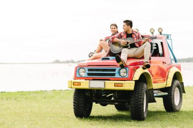 Asya Genç çift aşık bir araba üzerinde otururken gitar çalmak 