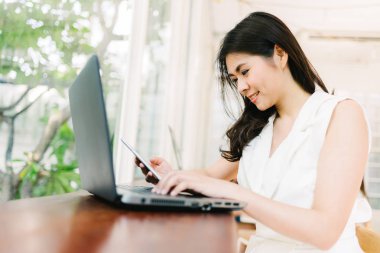  Asyalı kadın gülümseme laptop ile akıllı telefon telefon kullanırken 