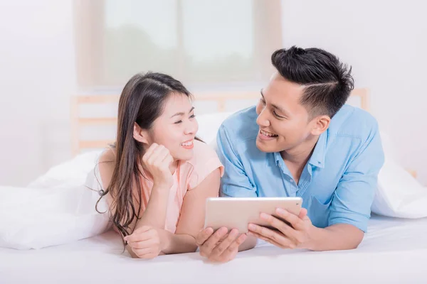 Asiatiska par Le och njuta av medan du tittar på tablett i sängen — Stockfoto
