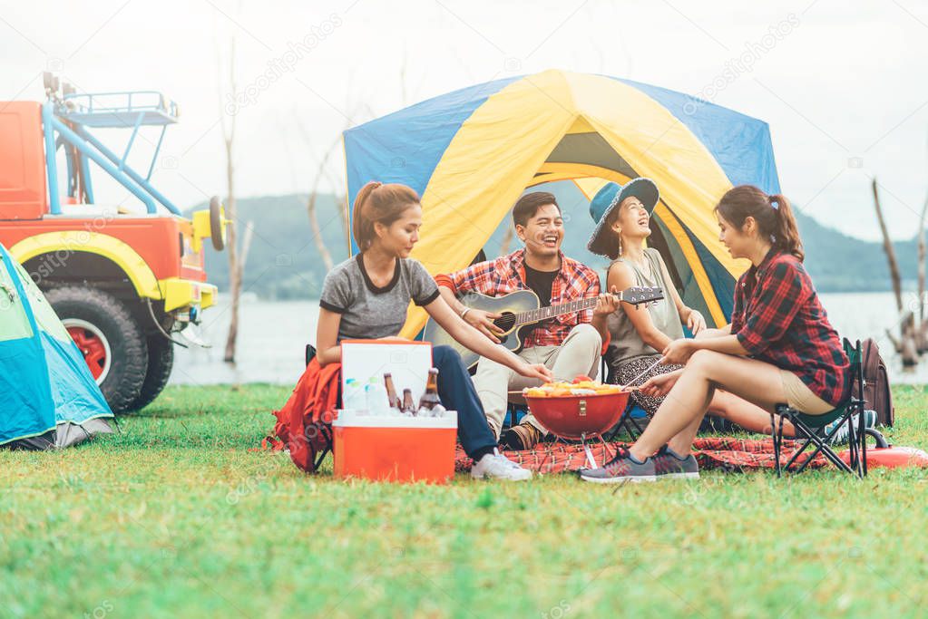 Asian friends having fun eating barbecue outdoor while camping